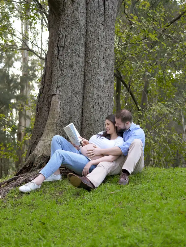 Expecting couple seated together beneath a tree