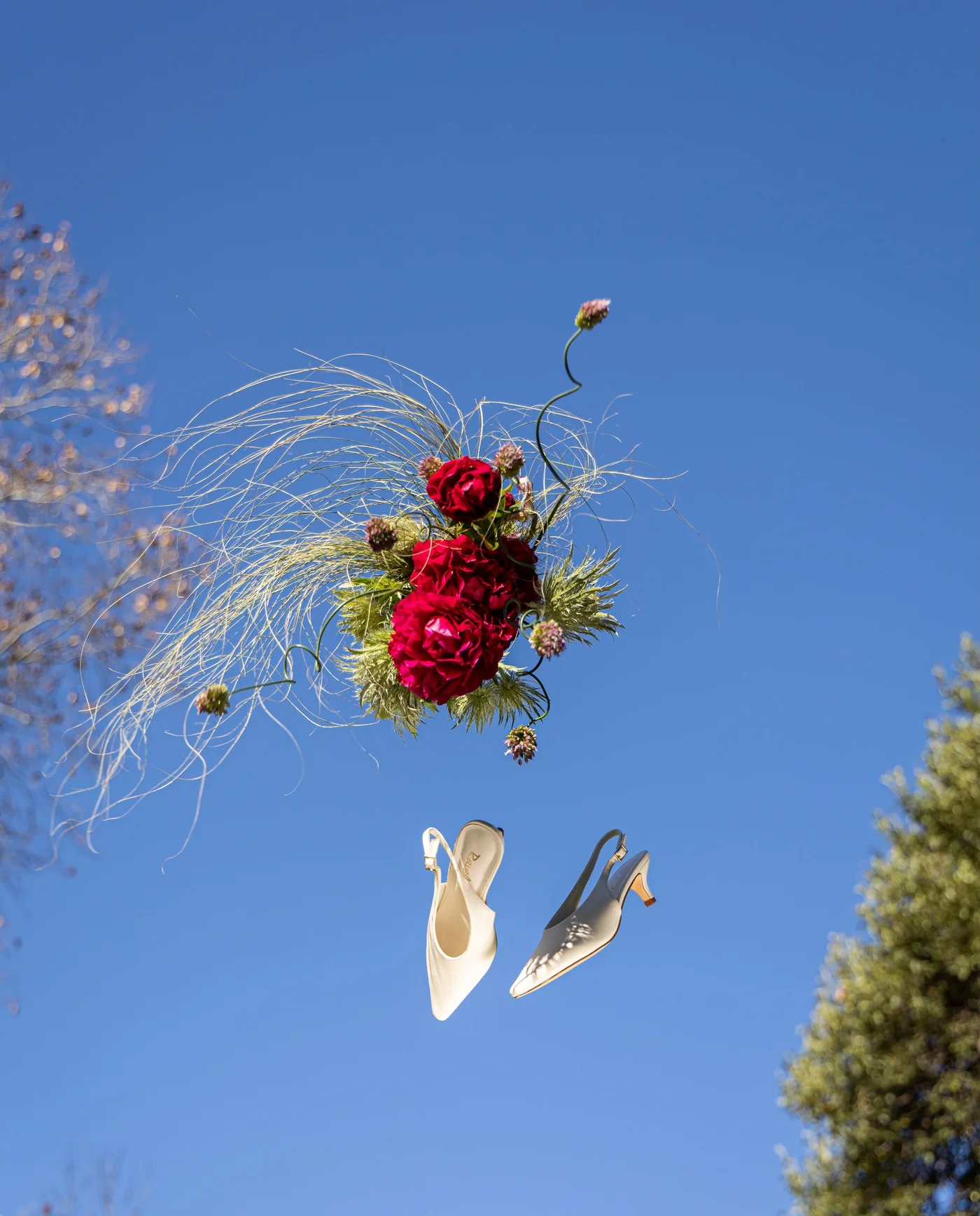 A red wedding bouquet and bridal shoes against a blue sky.